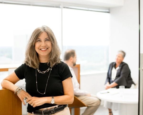A woman smiling at the camera with her colleagues in the conference room behind