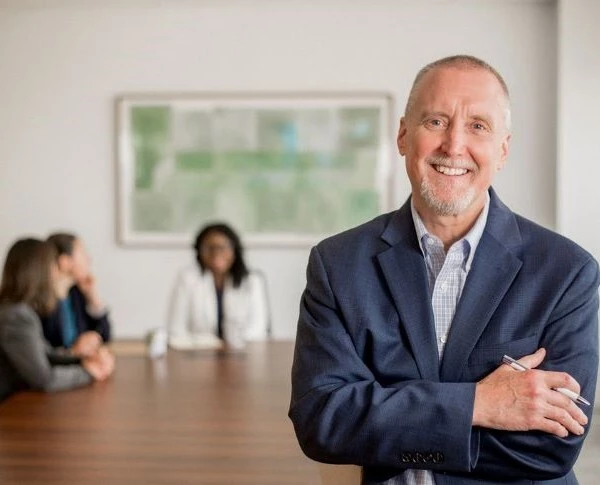 An attorney smiling at the camera while his team meets in the background