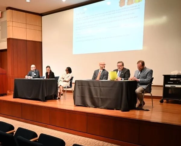 men and women in suits sit at two tables for a mock trial