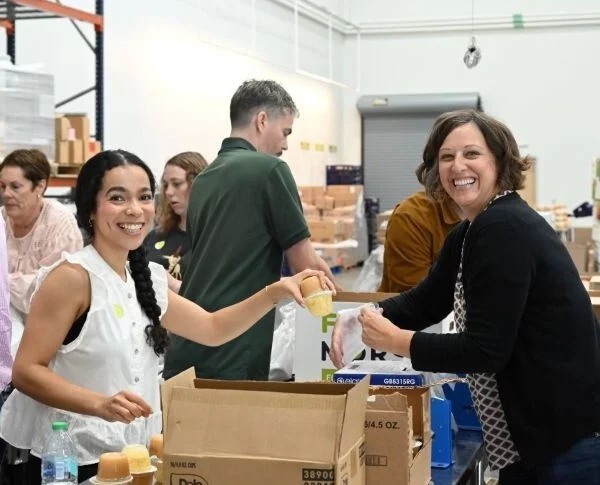 Two women pack boxes of food at a warehouse
